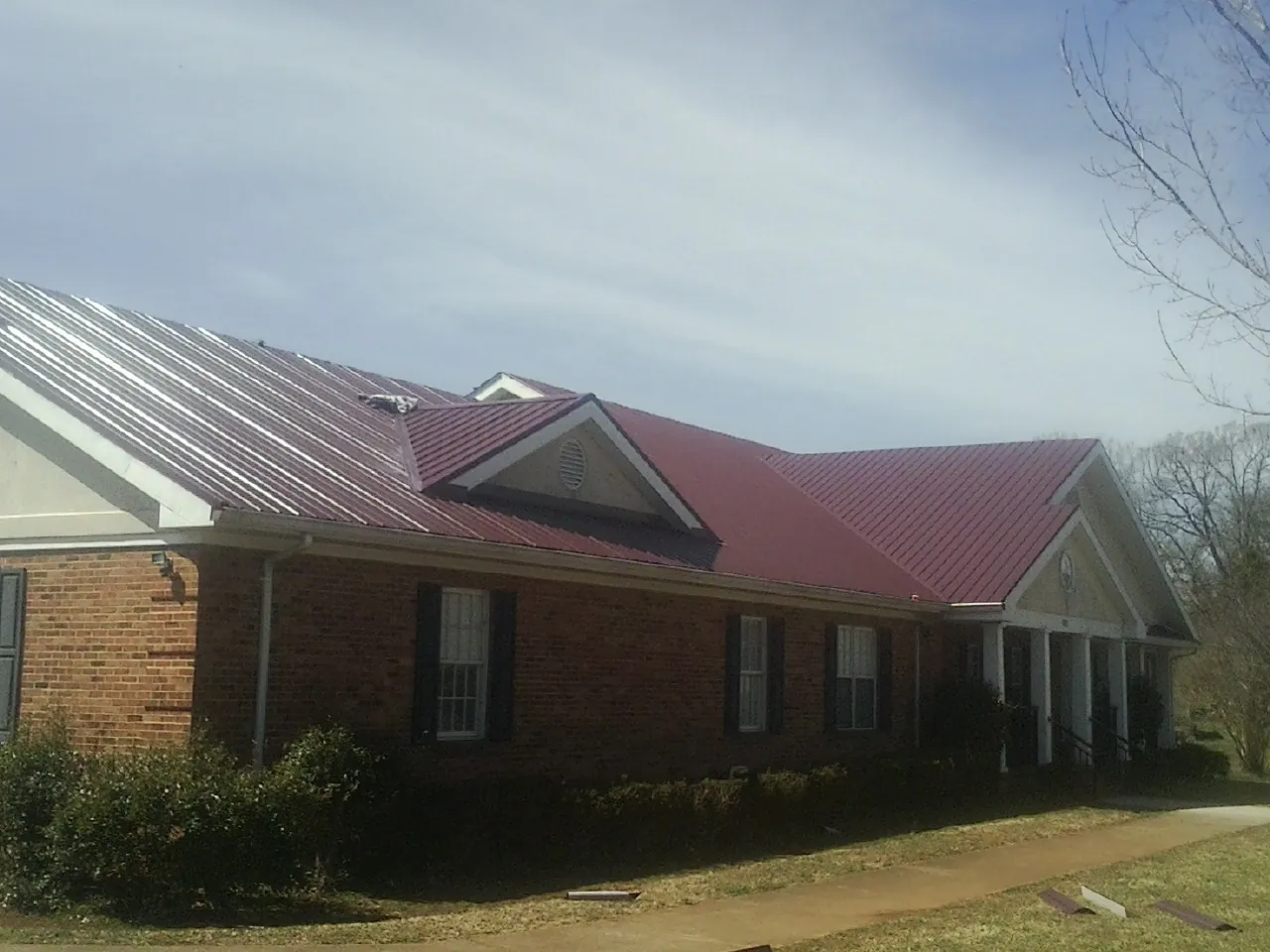 Red metal roof with gabled entries on a long brick building, from a Hail Damage Roof Repair job in East Wenatchee