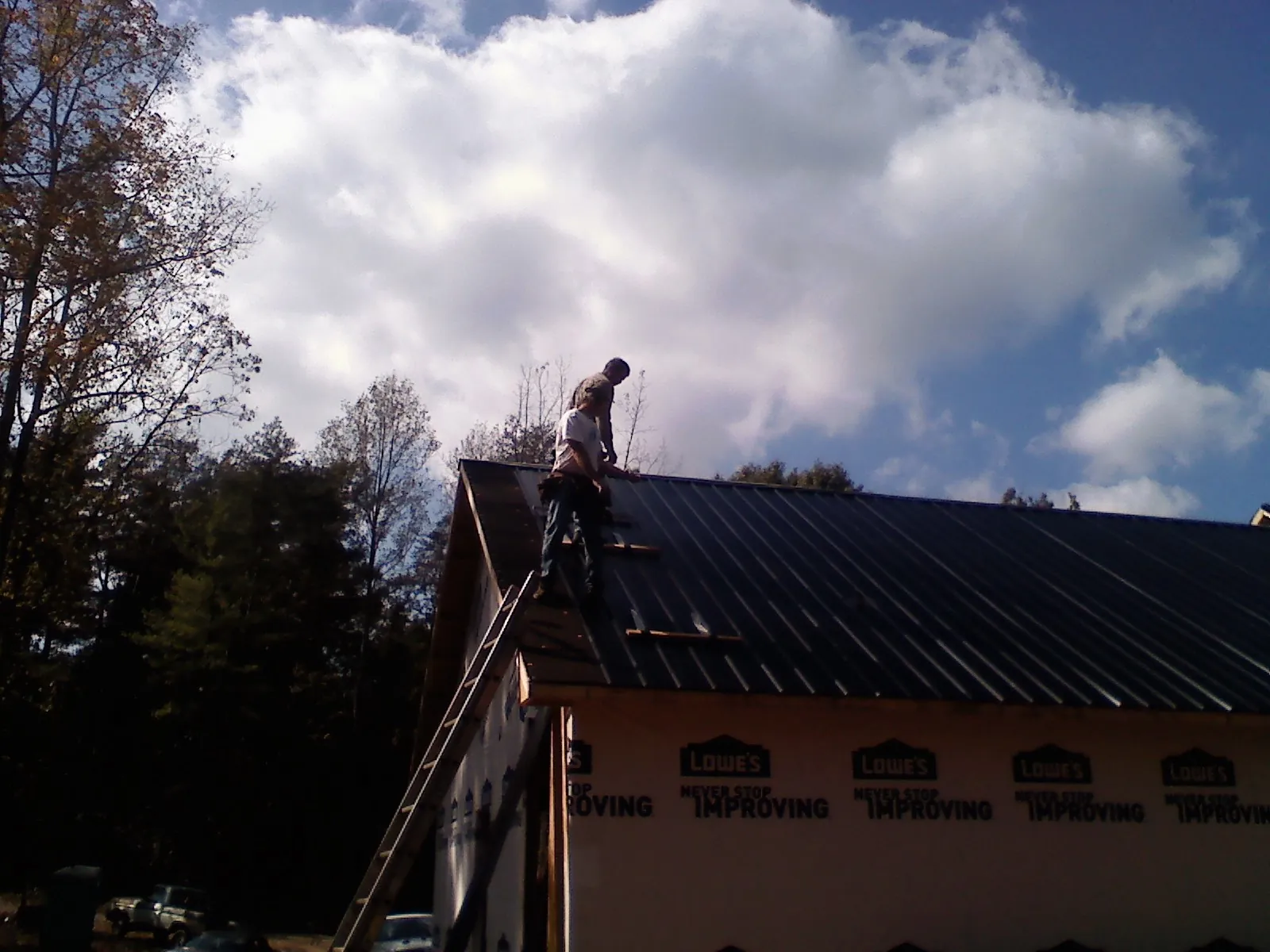 Roofer fastening dark metal panels high against a cloudy sky, from a Roof Inspection job in East Wenatchee