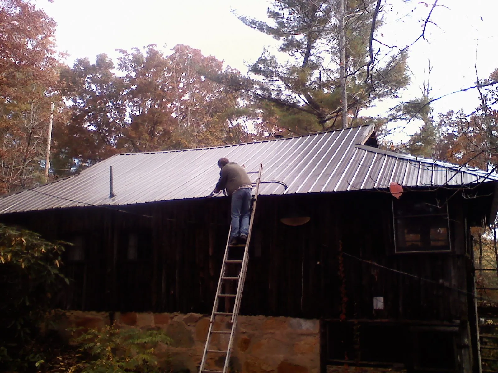 Roofer on a ladder working along the edge of a cabin metal roof in East Wenatchee
