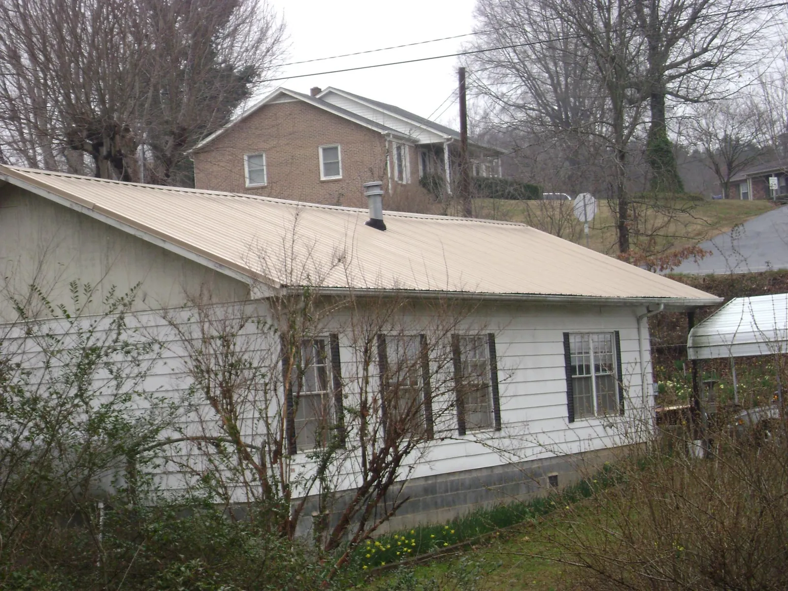Tan metal roof on a white sided house set into a hillside — Commercial Roofing by Roofing Brothers in East Wenatchee